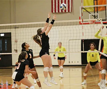 A Cedar Valley Volleyball player jumps to block a ball coming over the net