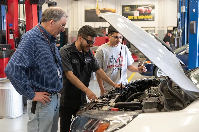 Students check on a car engine with their instructor