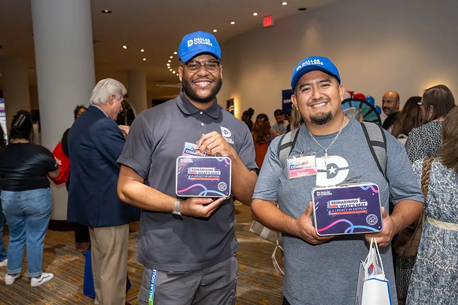 Two Dallas College employees pose with commemorative lunch boxes.