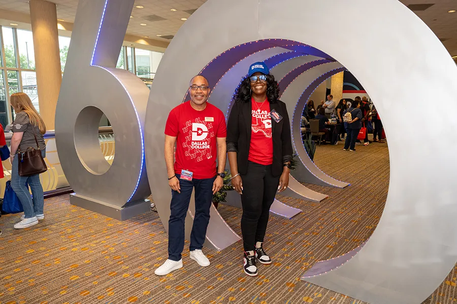 Two Dallas College employees pose in front of the 60th Anniversary sculpture.