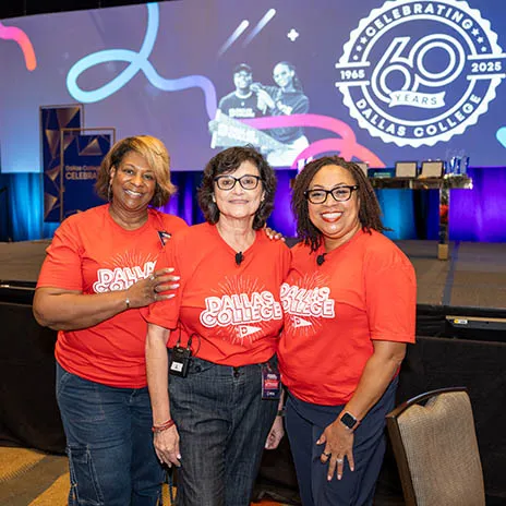 Three Dallas College employees pose in front of stage with backdrop showing the 60th Anniversary logo.