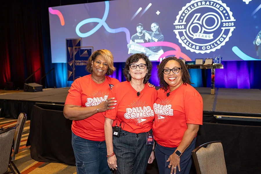 Three Dallas College employees pose in front of stage with backdrop showing the 60th Anniversary logo.