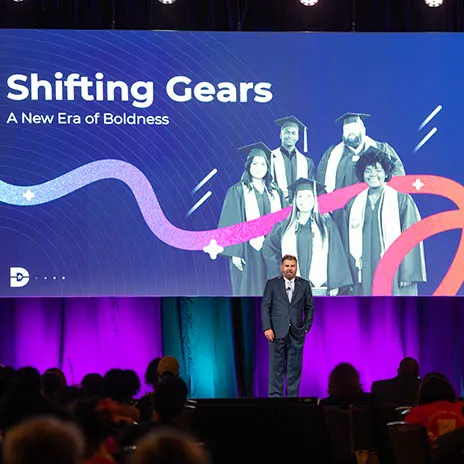 Dallas College chancellor on stage during Conference Day. A backdrop behind him reads, Shifting Gears, A New Era of Boldness.