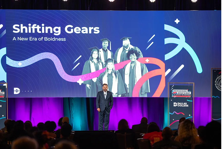 Dallas College chancellor on stage during Conference Day. A backdrop behind him reads, Shifting Gears, A New Era of Boldness.