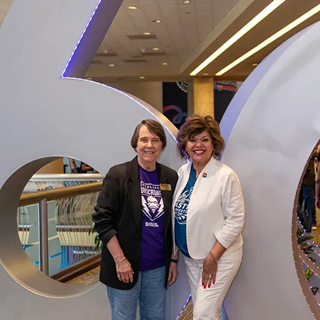 Two Dallas College employees pose in front of the 60th Anniversary sculpture.