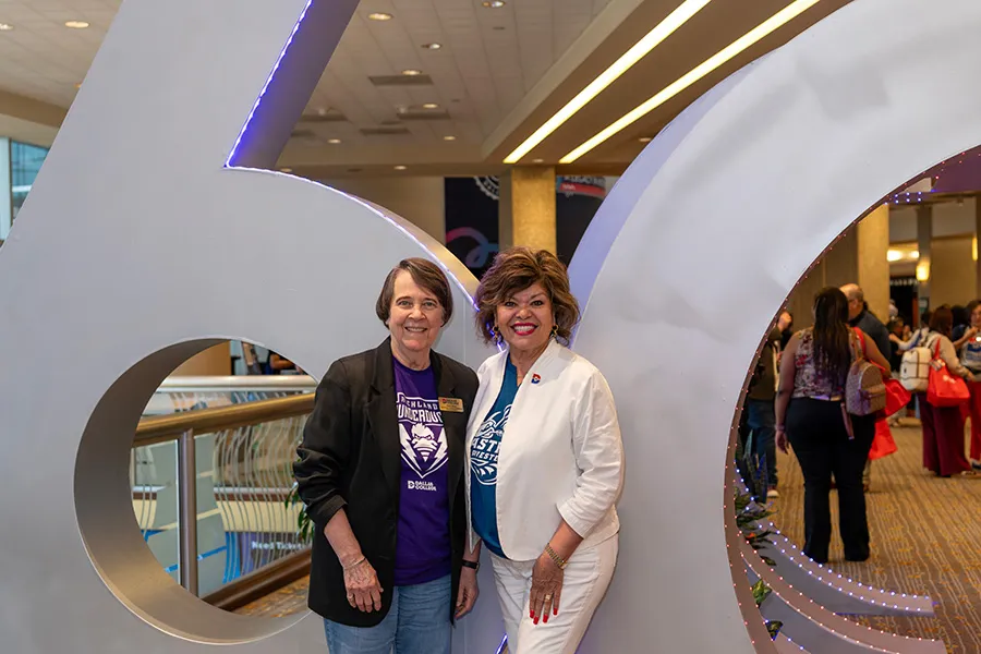 Two Dallas College employees pose in front of the 60th Anniversary sculpture.