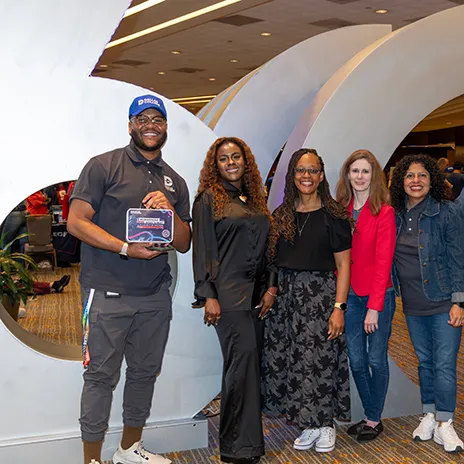 Five Dallas College employees pose in front of the 60th Anniversary sculpture. One is holding a commemorative lunch box.