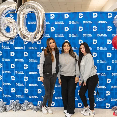 Three students pose in front of Dallas College backdrop and balloons.