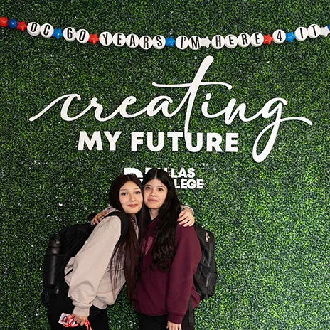 Two students pose in front of Instagram wall. Above is an oversized friendship bracelet reading: DC 60 YEARS I’M HERE 4 IT. Behind them the wall reads: creating my future with a Dallas College logo.