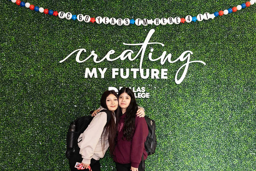 Two students pose in front of Instagram wall. Above is an oversized friendship bracelet reading: DC 60 YEARS I’M HERE 4 IT. Behind them the wall reads: creating my future with a Dallas College logo.