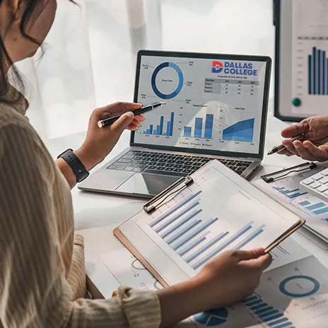 A woman looks over reports on a computer and desk