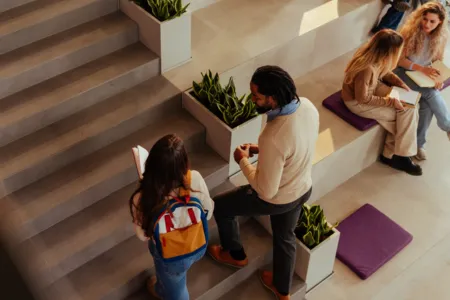 Students sit in a lobby while others walk up a set up stairs