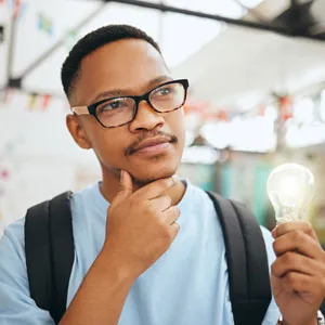 Student holding a lit light bulb with one hand and touching chin with the other