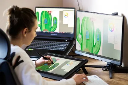 A female student works on a art project with a tablet and two monitors.