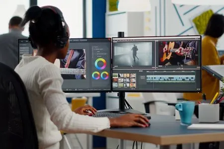 A student works on editing a video via their dual computer monitors.