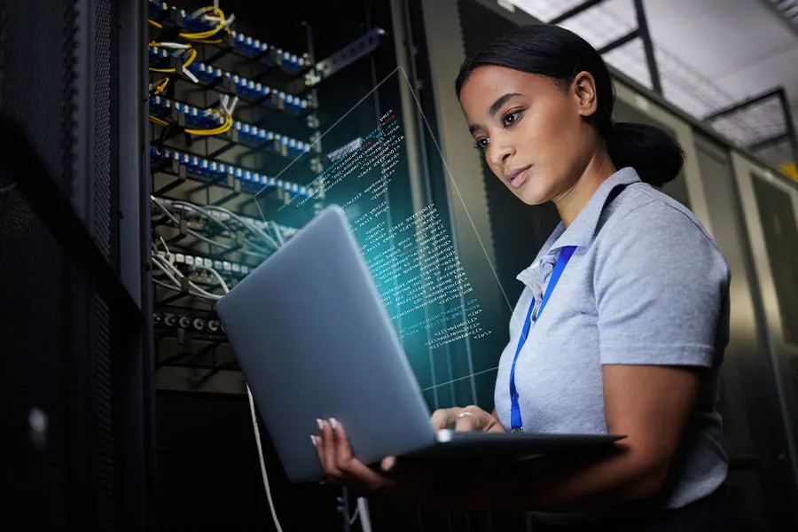 Woman sits at a laptop in front of network servers