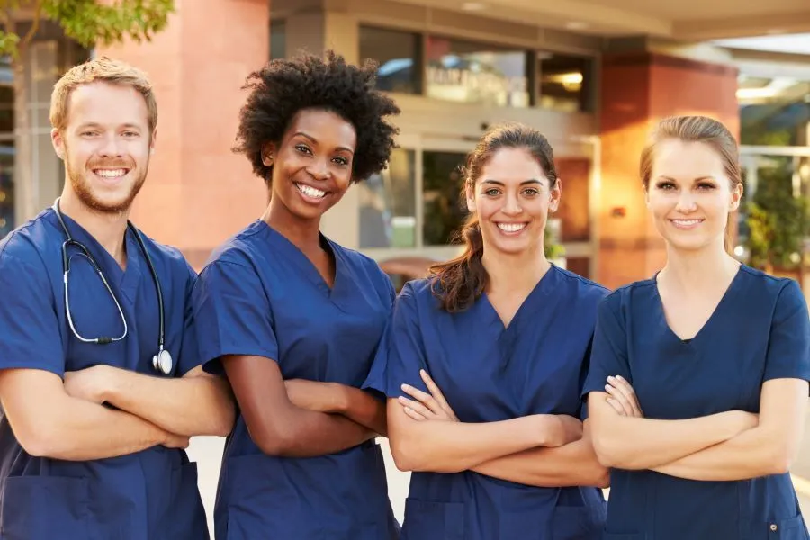 A group of nurses stand outside a hospital with their arms folded