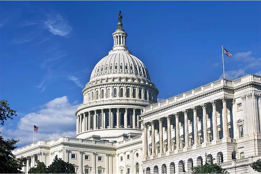 The U.S. Capitol building with its dome and statue is shown under a clear sky, with an American flag flying on the right.