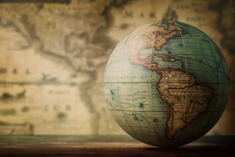 A globe focused on the Americas sits on a wooden surface, with a vintage sepia-toned world map in the background.