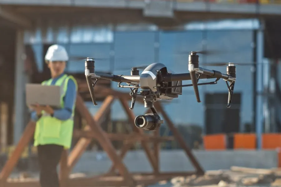 A drone flies over a construction site as a worker looks on