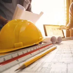 a yellow construction hat, a ruler, a pencil and blueprints