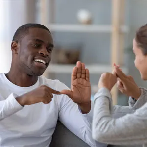 Smiling man and woman communicating using sign language in a cozy living room, conveying warmth and connection