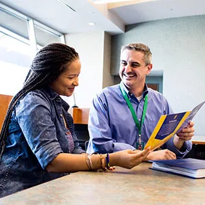 A man in a blue shirt showing a brochure to a woman at a table