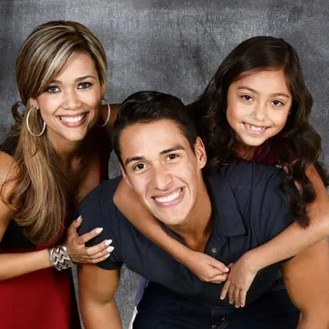 A smiling family of three poses against a gray background