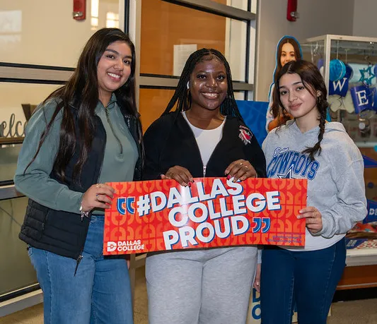 three girls standing and smiling together holding dallas college sign