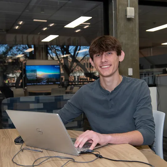 male student sitting in front of laptop smiling