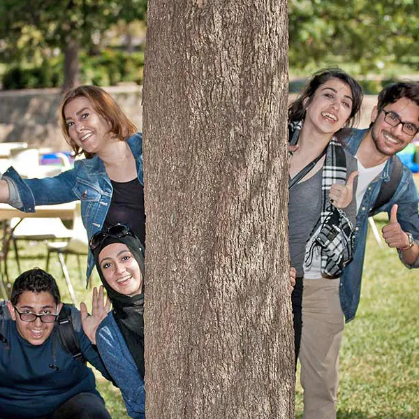 students leaning out from behind a tree and smiling