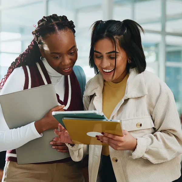 two female students looking at a notepad together and smiling