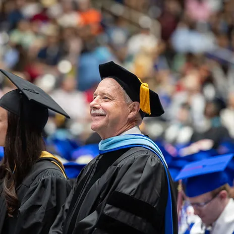 Dr. Mike Walker watches graduation while wearing his doctoral regalia