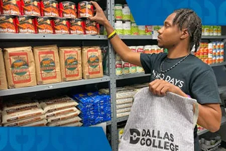 a man holding a Dallas College bag selects a can of food from well-stocked shelves
