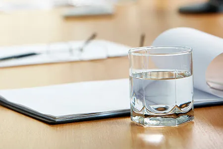 a close-up of a glass of water and pad of paper on a conference table