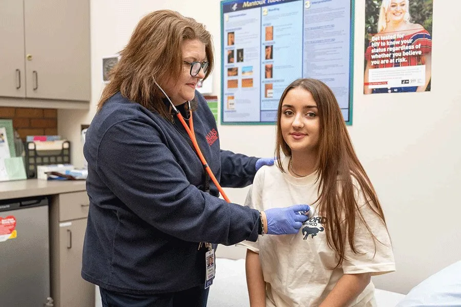 a health care worker holds a stethoscope against a young woman's chest