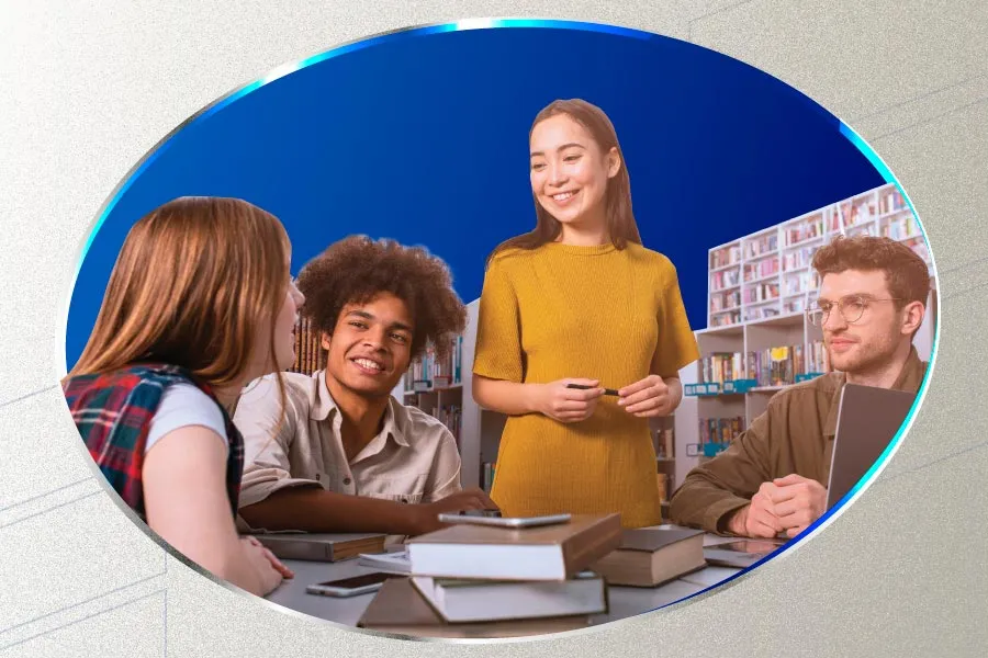 a group of students sit or stand around a table with a pile of books and a phone on it