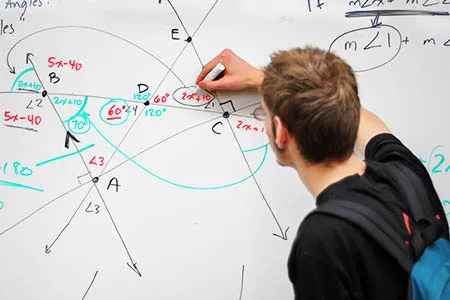 a student writes math equations on a white board