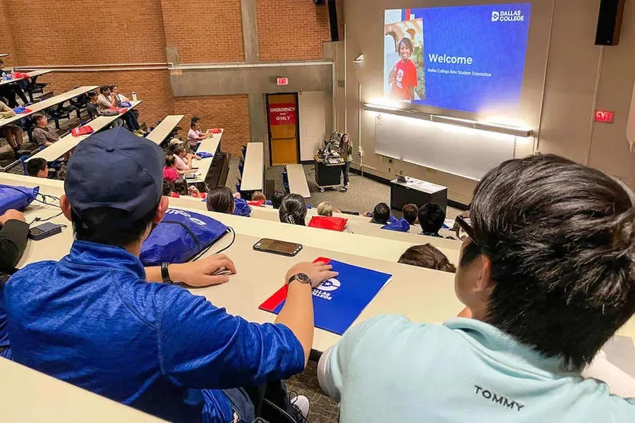 students sit in a large lecture hall looking at a welcome message on a large screen