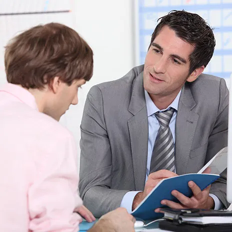 A Dual Credit instructor and a student are discussing a blue folder at a table