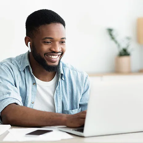 Student using a laptop at a desk with papers, phone, and a plant.