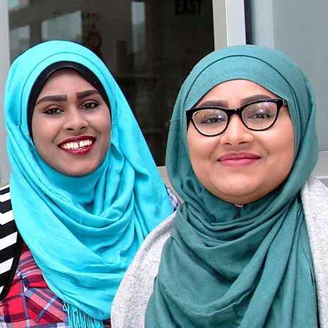 Two individuals wearing turquoise and teal hijabs, standing close together.
