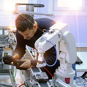 A person works on an assembly line with a robot arm assisting