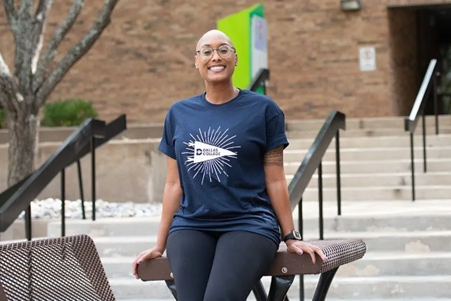 Qualonda Bennett leaning on a table, with a building of a Dallas College campus in the background.