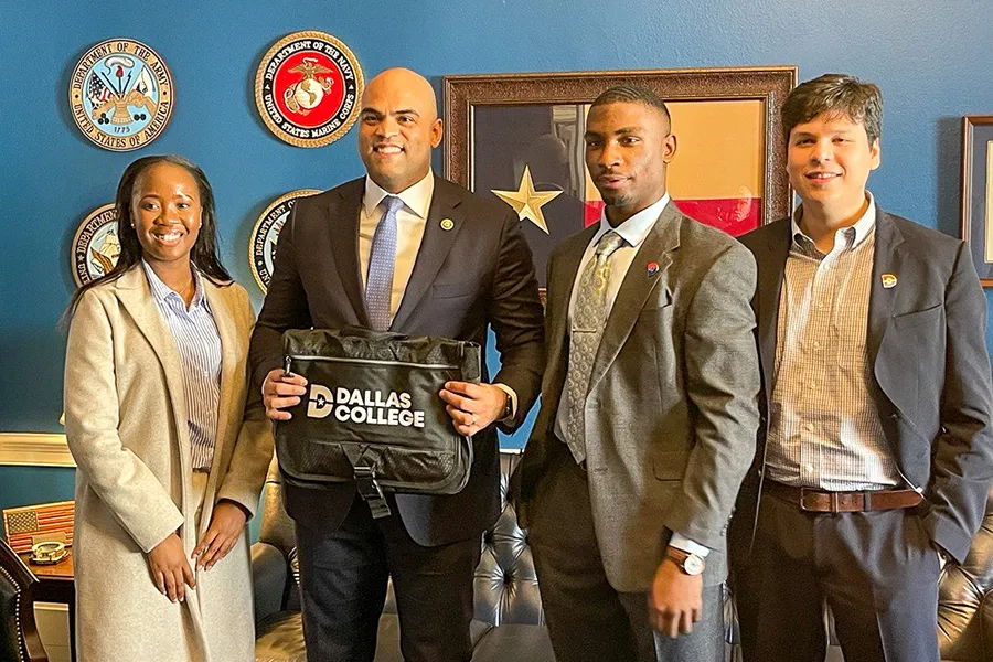Dallas College students and politicans take a picture while a politician holds a Dallas College laptop bag.