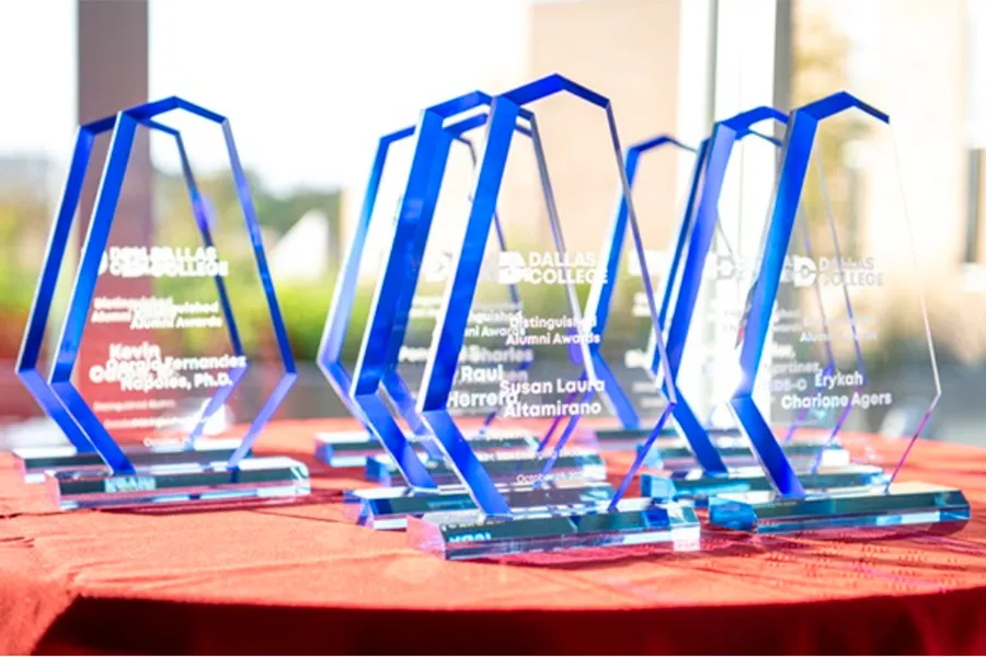 Alumni awards that are clear with a blue border sit on a red, circular table.