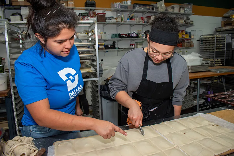 Maricsa Trejo, founder of La Casita Bakeshop, stands at the front of a culinary classroom demonstrating baking techniques to students gathered around a worktable.
