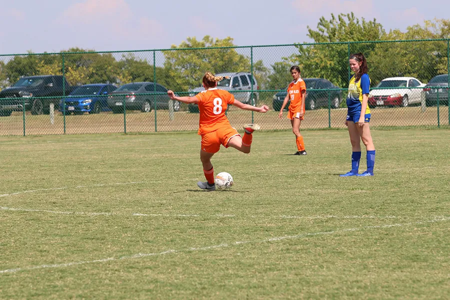 Women soccer player kicking a soccer ball. Two soccer players watch her.