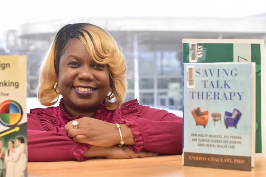 Nykesha rests her arms on a table between several books in a library. A book titled 