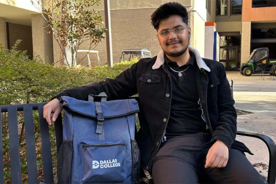 Osvaldo sitting on a bench with a Dallas College bag on campus